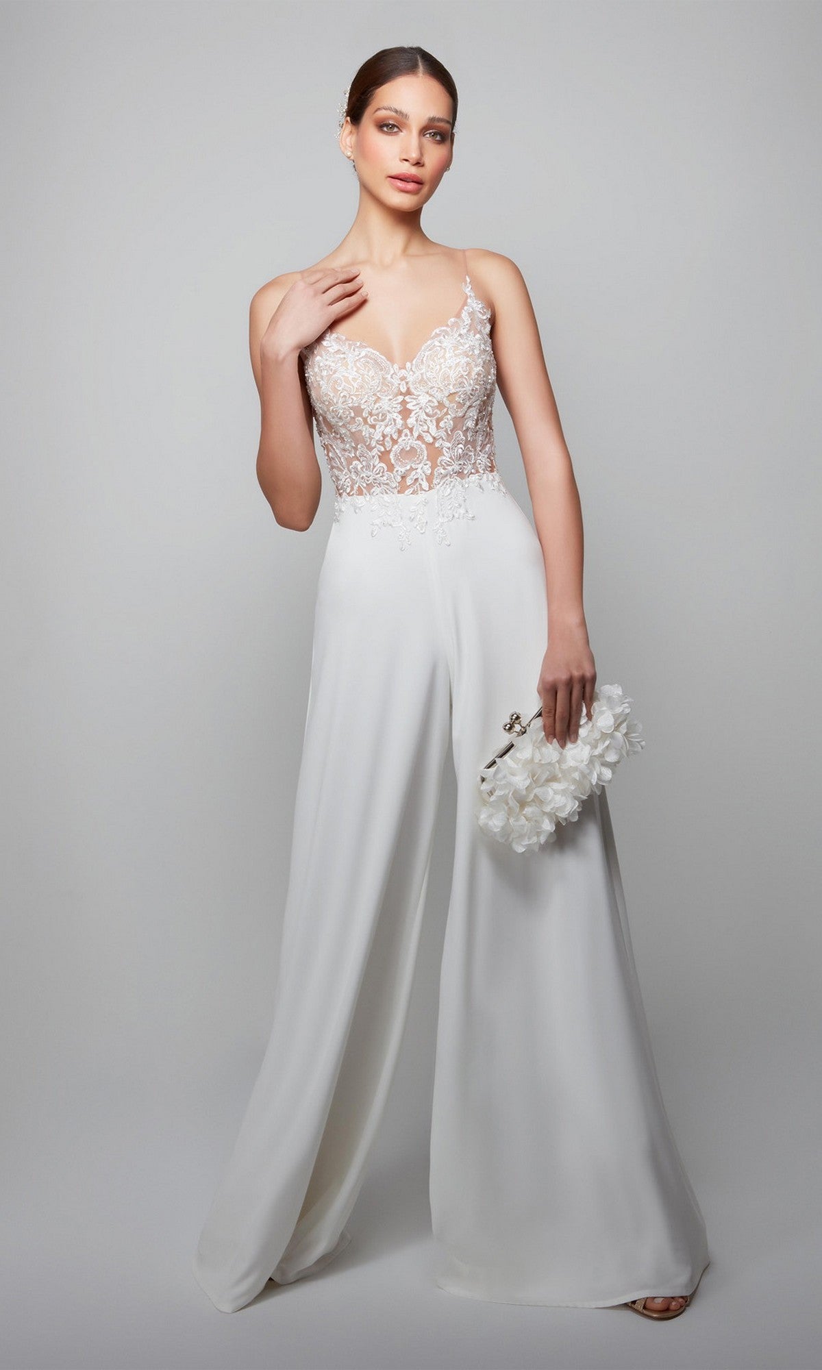 Woman models the Long White Jumpsuit: Alyce 70017 with a white lace bodice and wide-leg pants, holding a white floral clutch against a light gray background.